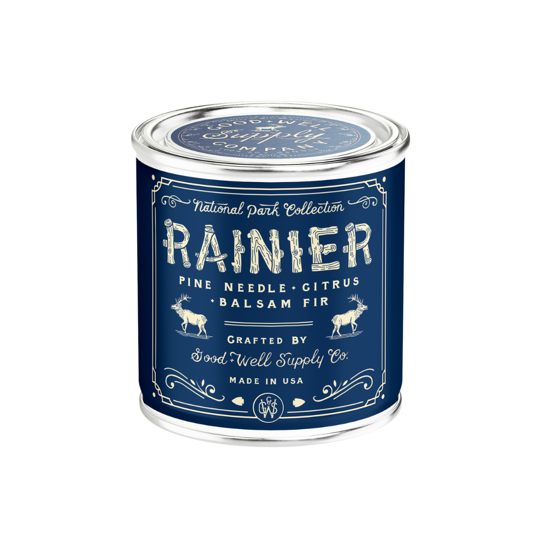 Candle in a blue container tin labeled 'Rainier' with decorative text on a white background