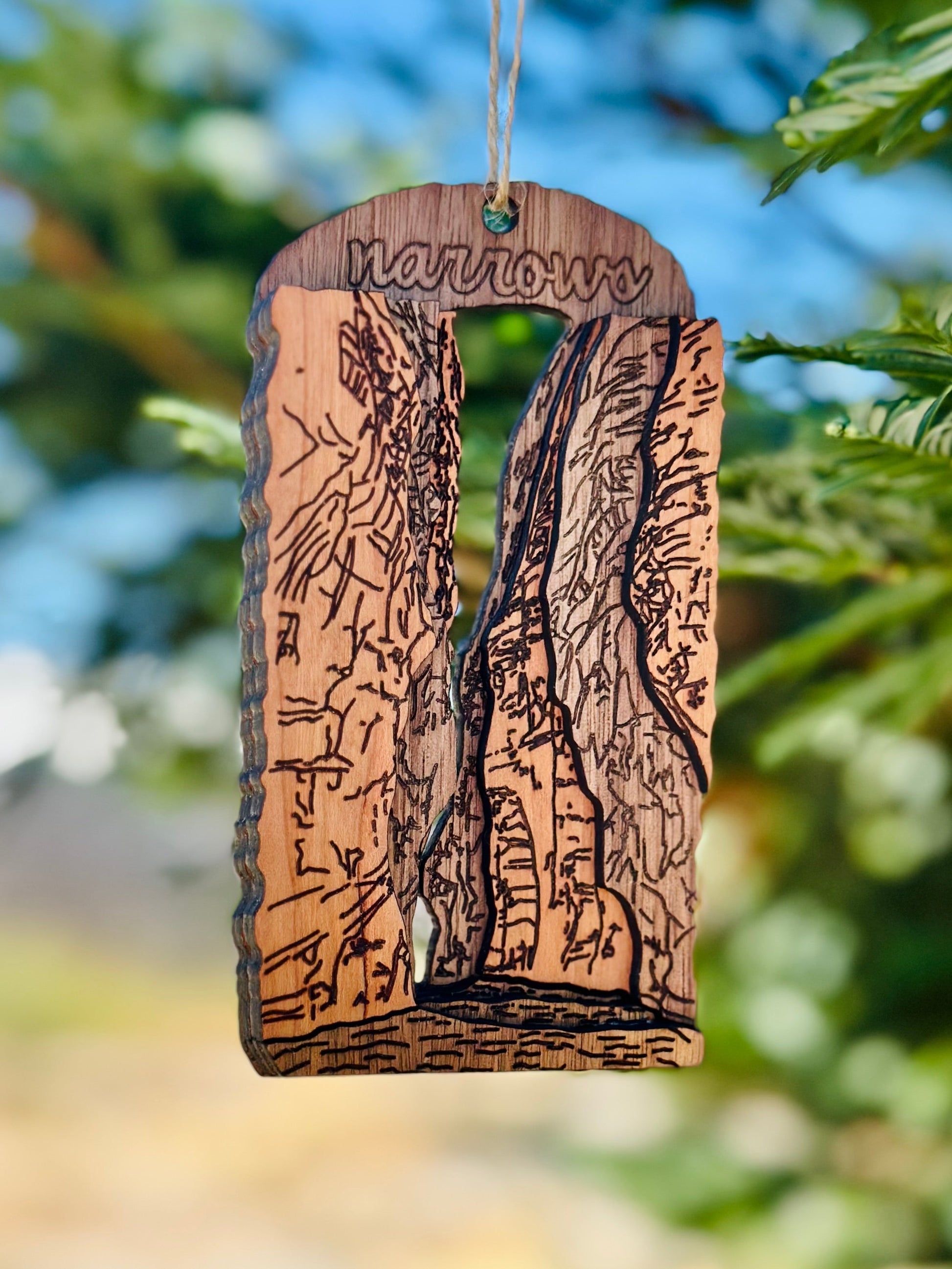 Wooden ornament with laser-cut design of the Narrows in Zion National Park against a blurred natural background