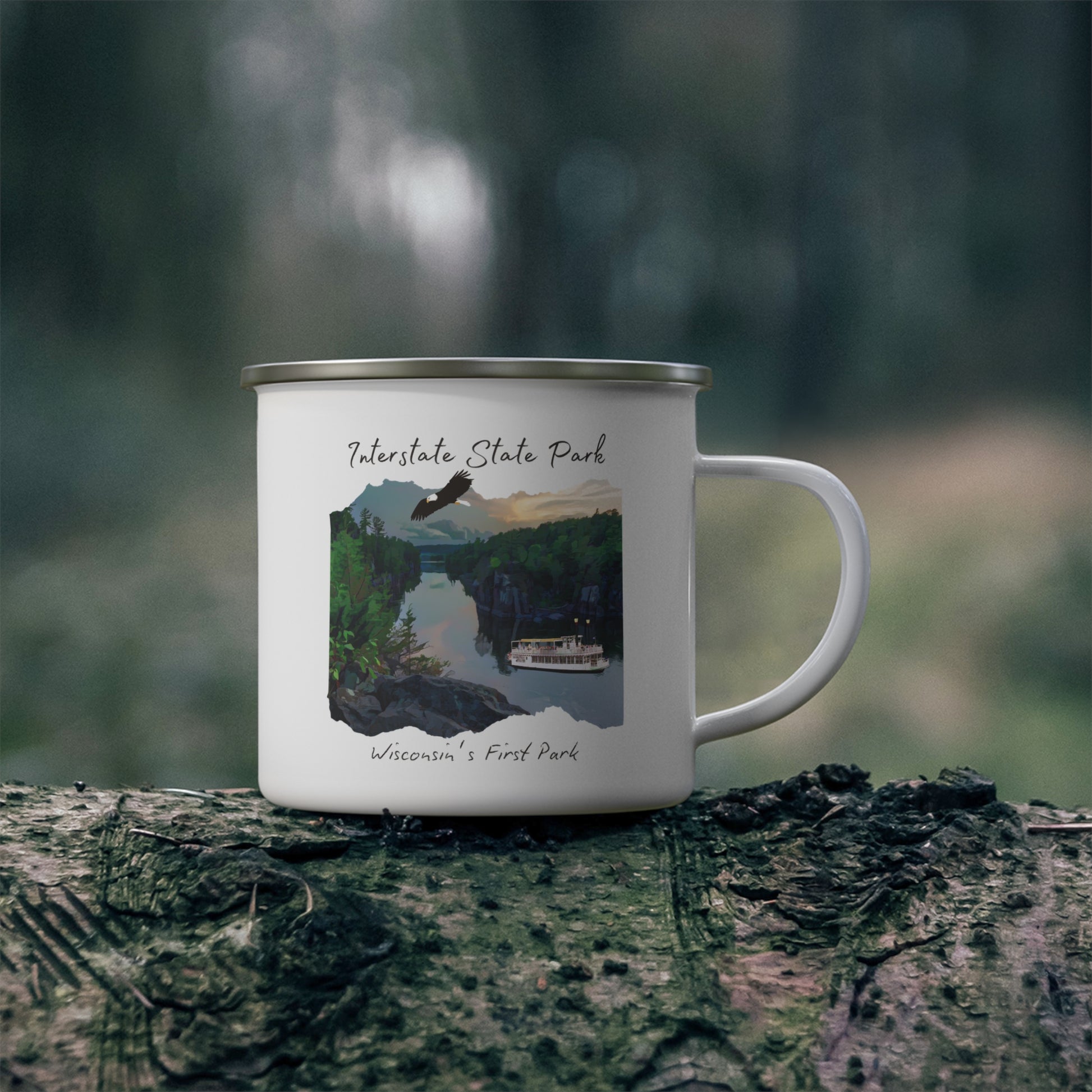 White enamel mug depicting the St Croix River at sunset with an eagle flying above and a paddle wheel boat on the river.  Photo background: mug sitting on a log in the woods.