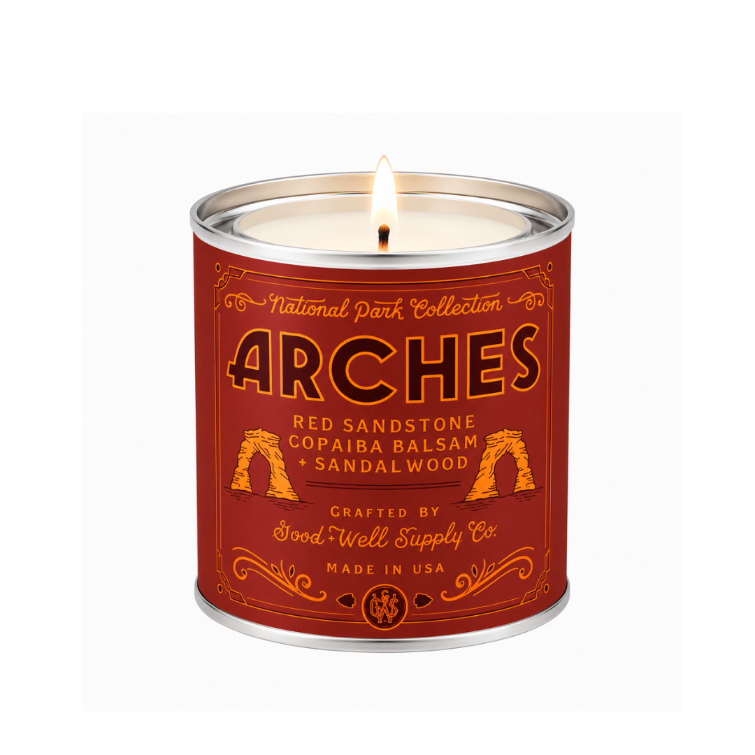 A lit metal tin candle from the National Park Collection by Good Well Supply Co., featuring a red label with gold and black text and imagery of red sandstone arches, set against a plain white background.