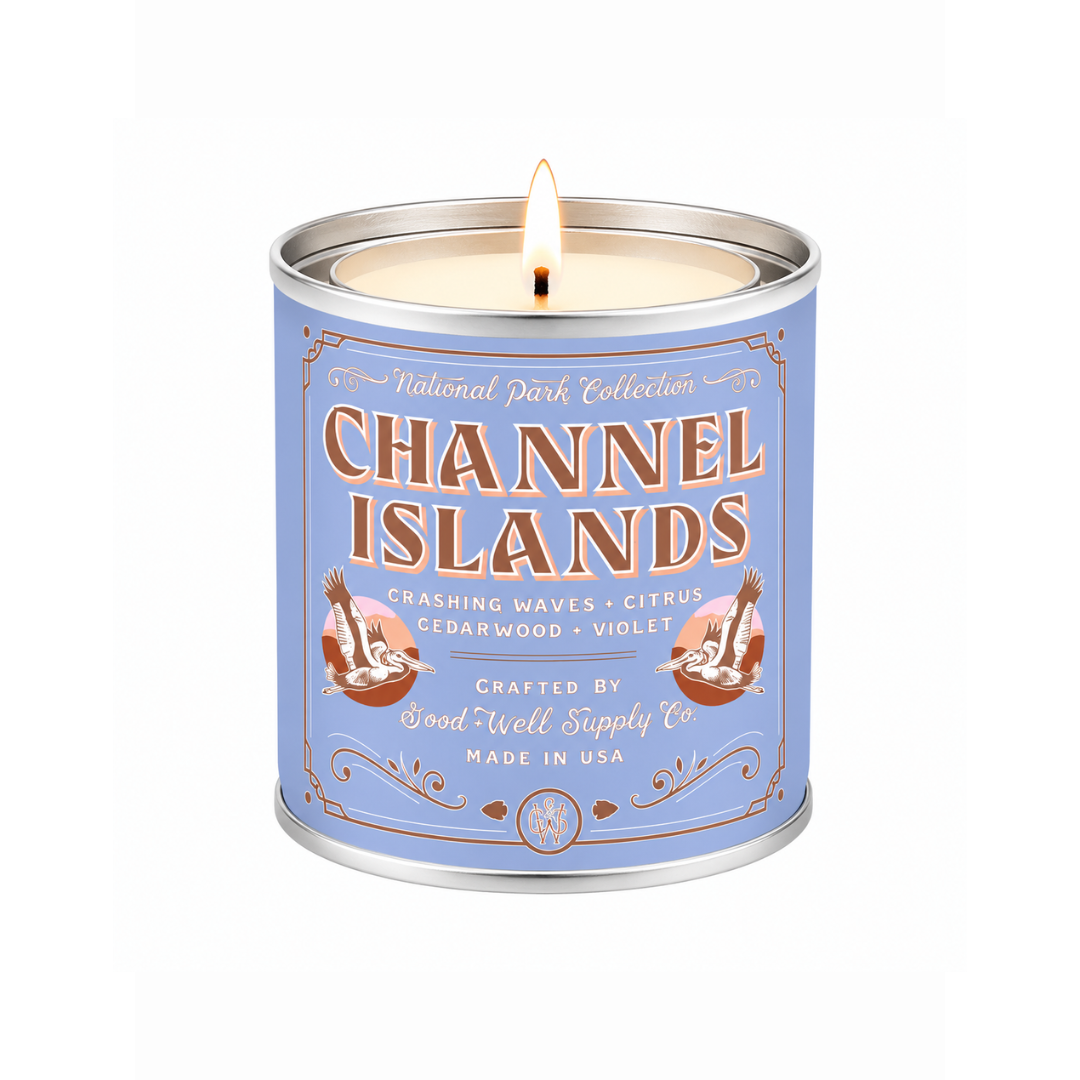 A lit scented candle in a cylindrical metal tin with a light blue label reading 'Channel Islands' and 'National Park Collection.' The candle is shown on a clean white background.