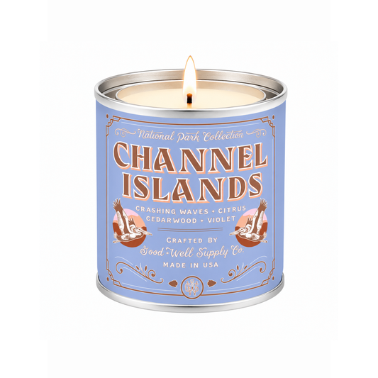 A lit scented candle in a cylindrical metal tin with a light blue label reading 'Channel Islands' and 'National Park Collection.' The candle is shown on a clean white background.