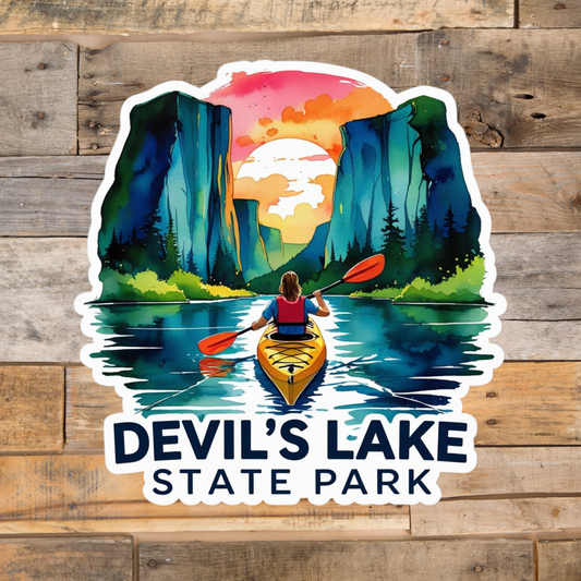 Watercolor style sticker featuring a kayaker on a lake surrounded by towering rock bluffs, a vivid sunset and the text Devil’s Lake State Park.  Photo background: rustic barn wood. 