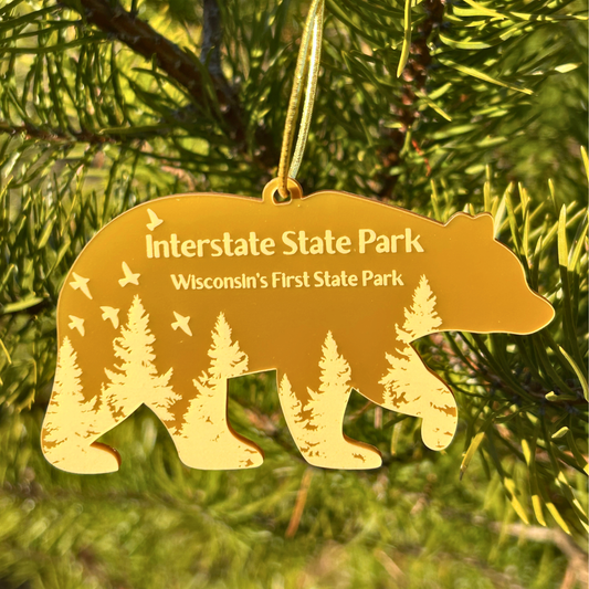 Gold bear-shaped ornament with 'Interstate State Park' text and forest scene on a green tree background