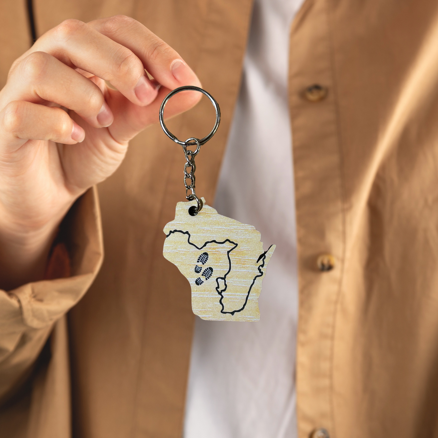 Acrylic Wisconsin shaped keychain with the Ice Age Trail route engraved on it and a pair of boot tracks.  Photo background: person holding key chain.