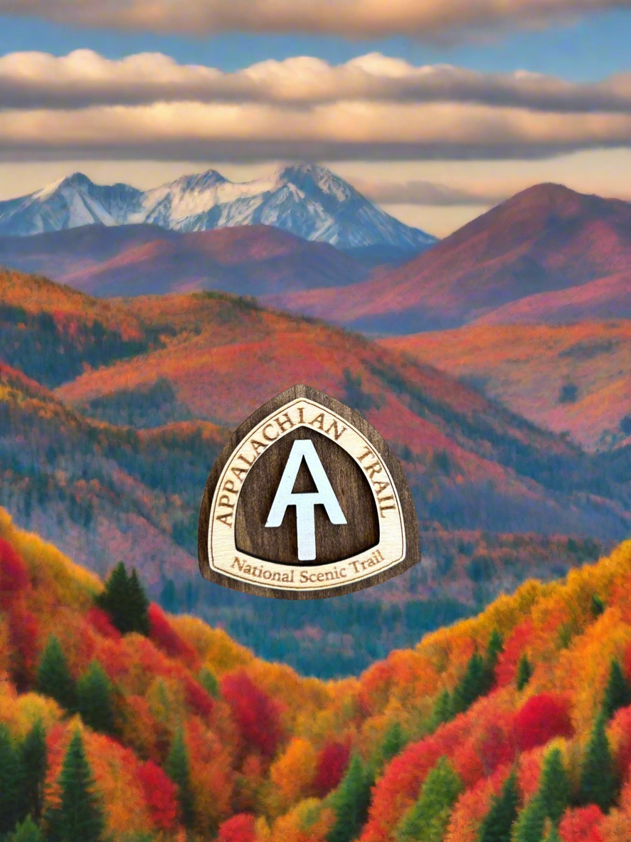 National scenic trail shaped magnet with Appalachian Trail National Scenic Trail, and white AT text symbol.  Background is mountains during fall leaf color.