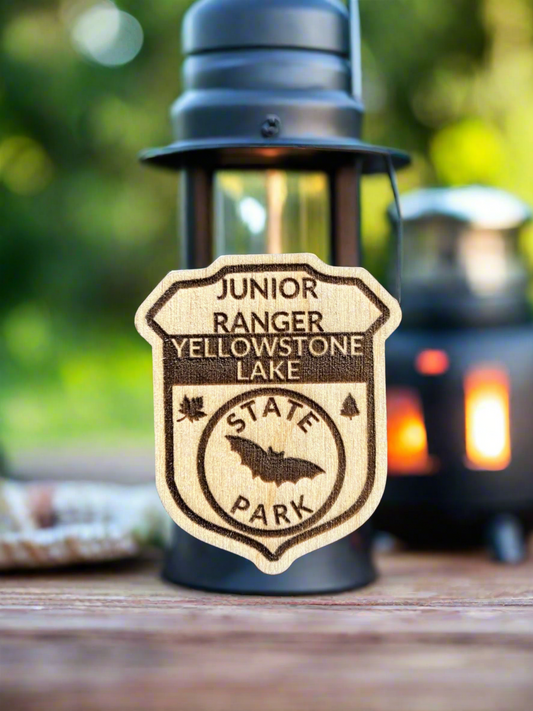 Wood badge shaped junior ranger pin with text Yellowstone Lake State Park and bat icon. 