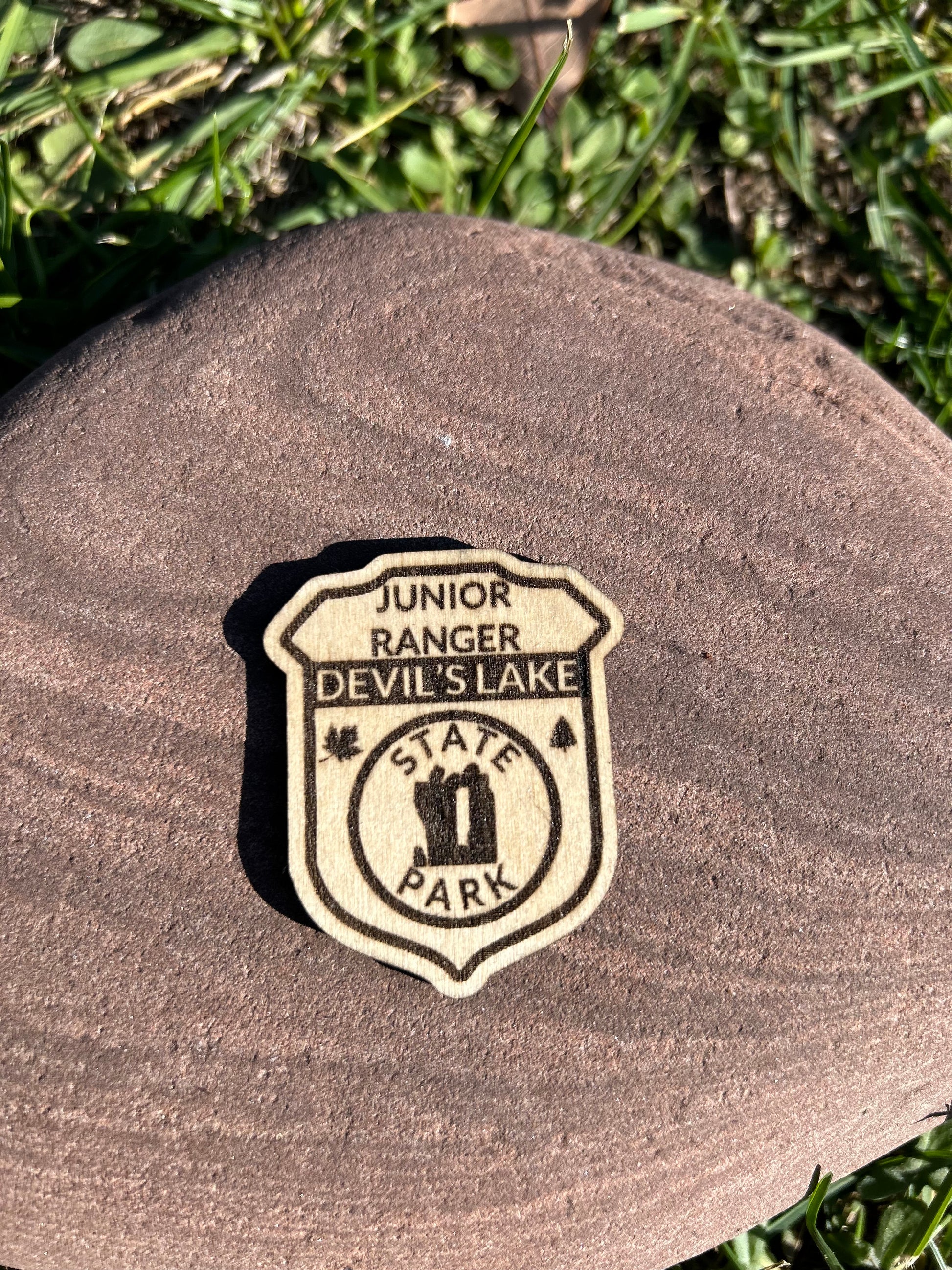 Wood badge shaped junior ranger pin with text Devil's Lake State Park and Devil's Doorway symbol. 