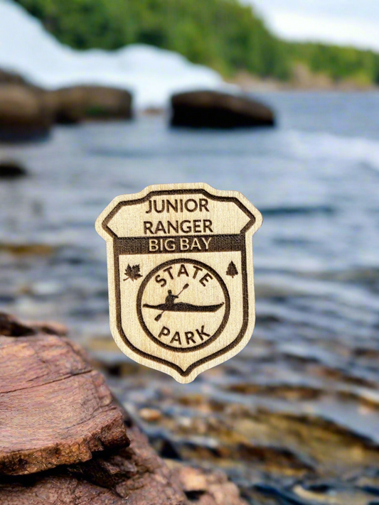 Wood Junior ranger badge depicting Big Bay State Park with a Kayak Symbol. 