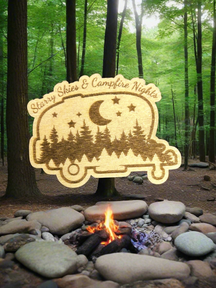 Wood magnet in the shape of a camper with a forest and starry night design and the text "starry Skies and Campfire Nights". 