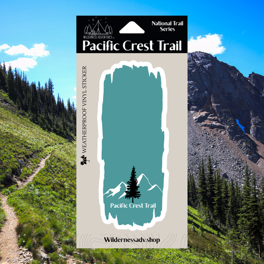 Blue and white Pacific Crest Trail vinyl sticker with the text “Pacific Crest Trail” and a tree and mountain design.  Photo background is a scenic view with mountains and trees.