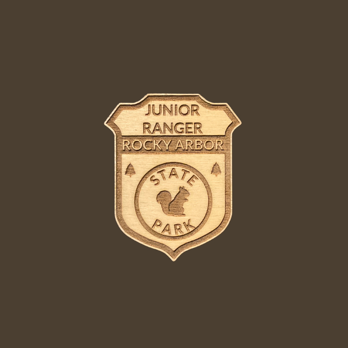 Wood badge featuring the text: “Junior Ranger Rocky Arbor State Park” and a squirrel icon on a brown background.