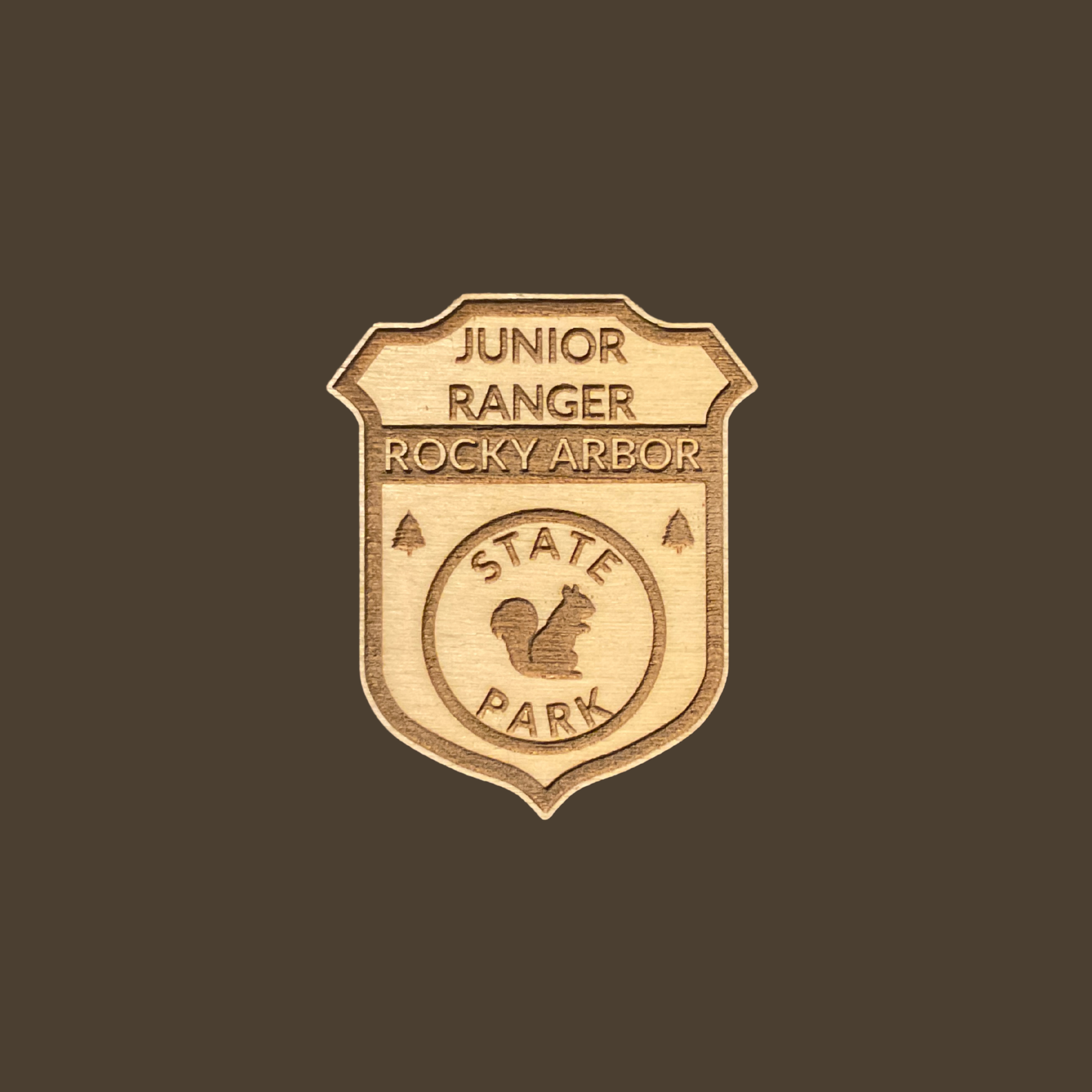 Wood badge featuring the text: “Junior Ranger Rocky Arbor State Park” and a squirrel icon on a brown background.