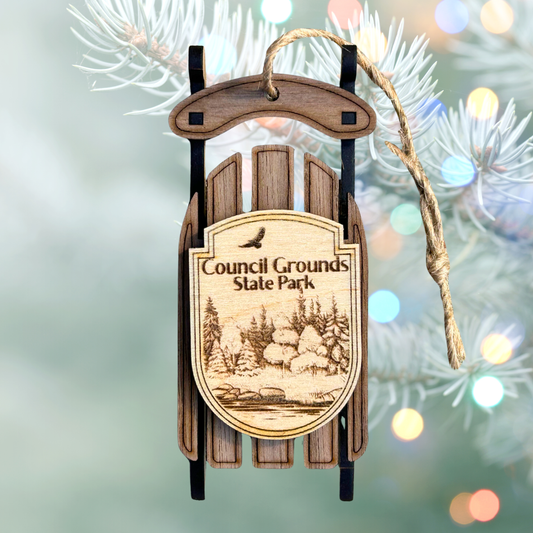 Wooden sled ornament with 'Council Grounds State Park' text and illustration, hanging on a Christmas tree.