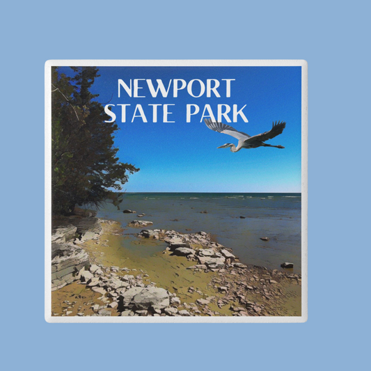Ceramic coaster depicting the rugged shoreline of Newport State Park and a great blue heron flying in the sky.  Features the text: Newport State Park.