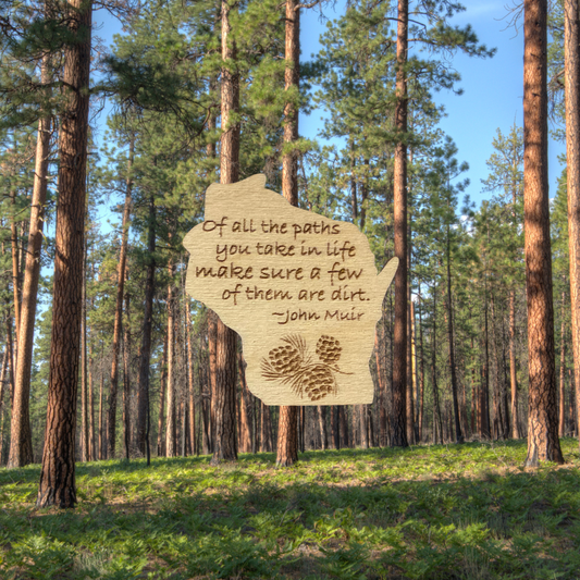 Wood Wisconsin shaped magnet with the John Muir quote: “of all the paths you take in life, make sure a few of them are dirt.”  Background of tall pine trees.
