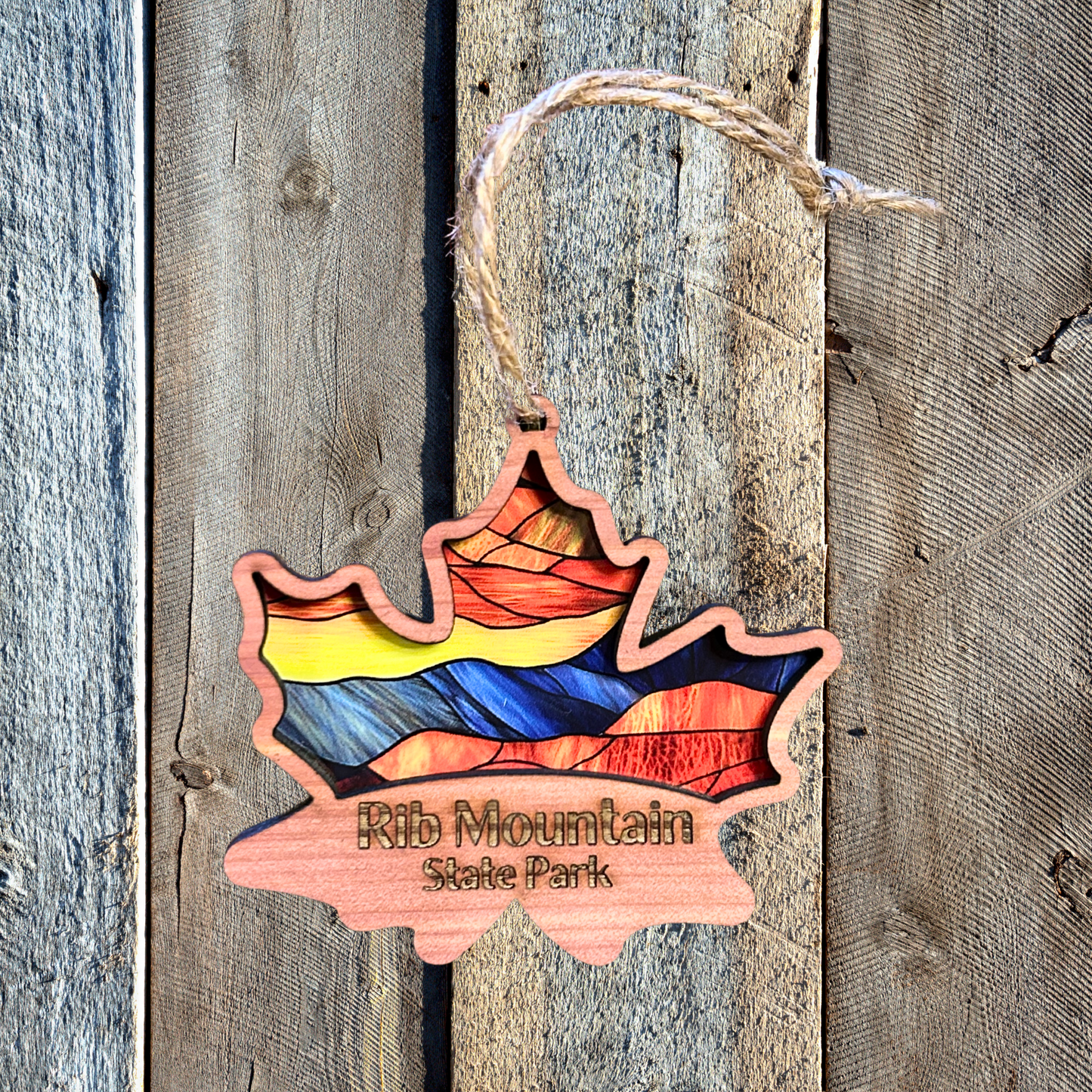 Cedar wood maple leaf ornament with stained glass appearance and the text “Rib Mountain State Park.”  Photo Background: Barnwood.