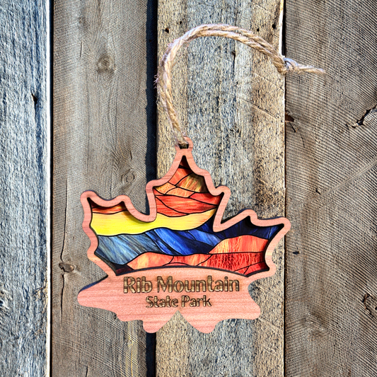 Cedar wood maple leaf ornament with stained glass appearance and the text “Rib Mountain State Park.”  Photo Background: Barnwood.