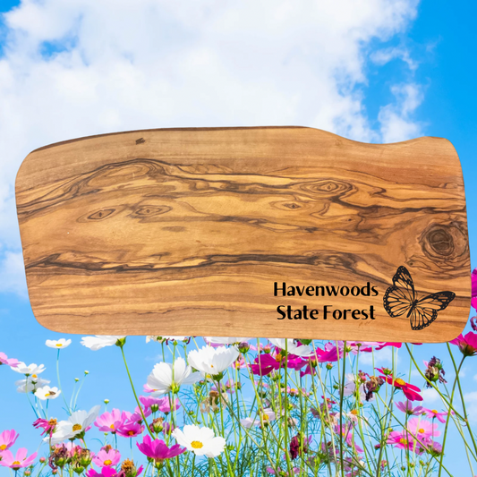 Olive wood serving board with the text “Havenwoods State Forest” and a butterfly icon.  Photo background: bright flowers and blue sky.