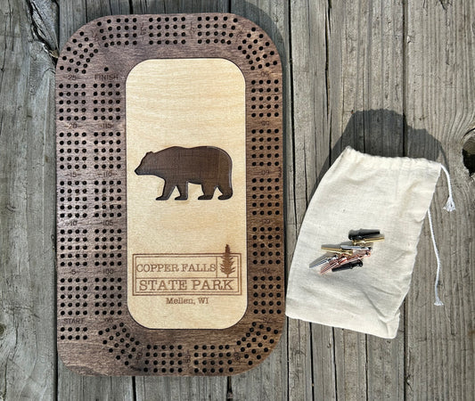 Wood cribbage board with a bear shaped cutout and Copper Falls State Park Text.  With eight metal pins. 