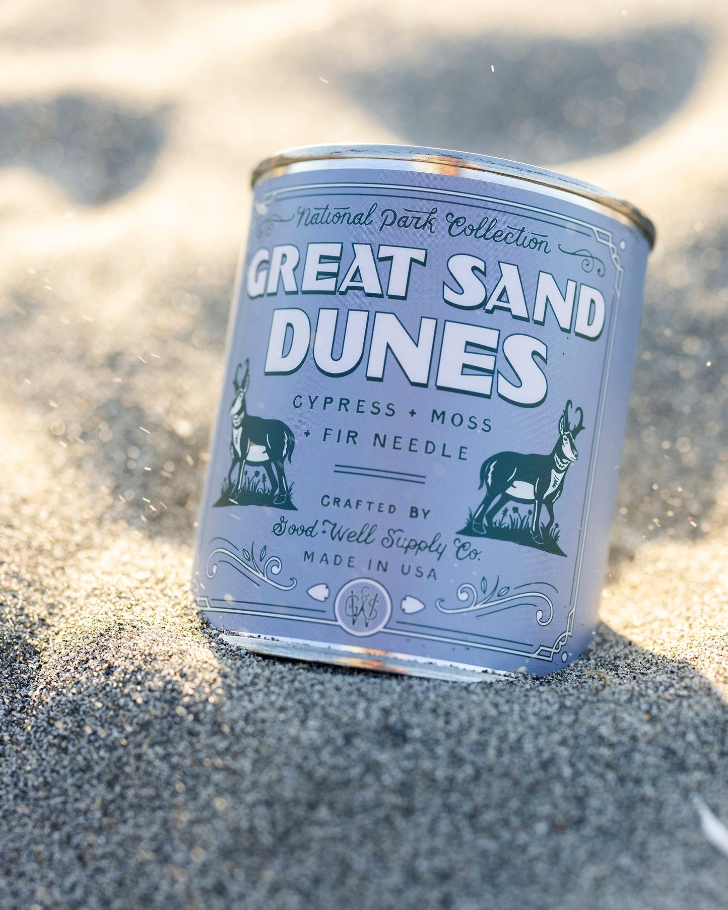 Candle tin labeled 'Great Sand Dunes' on a sandy surface