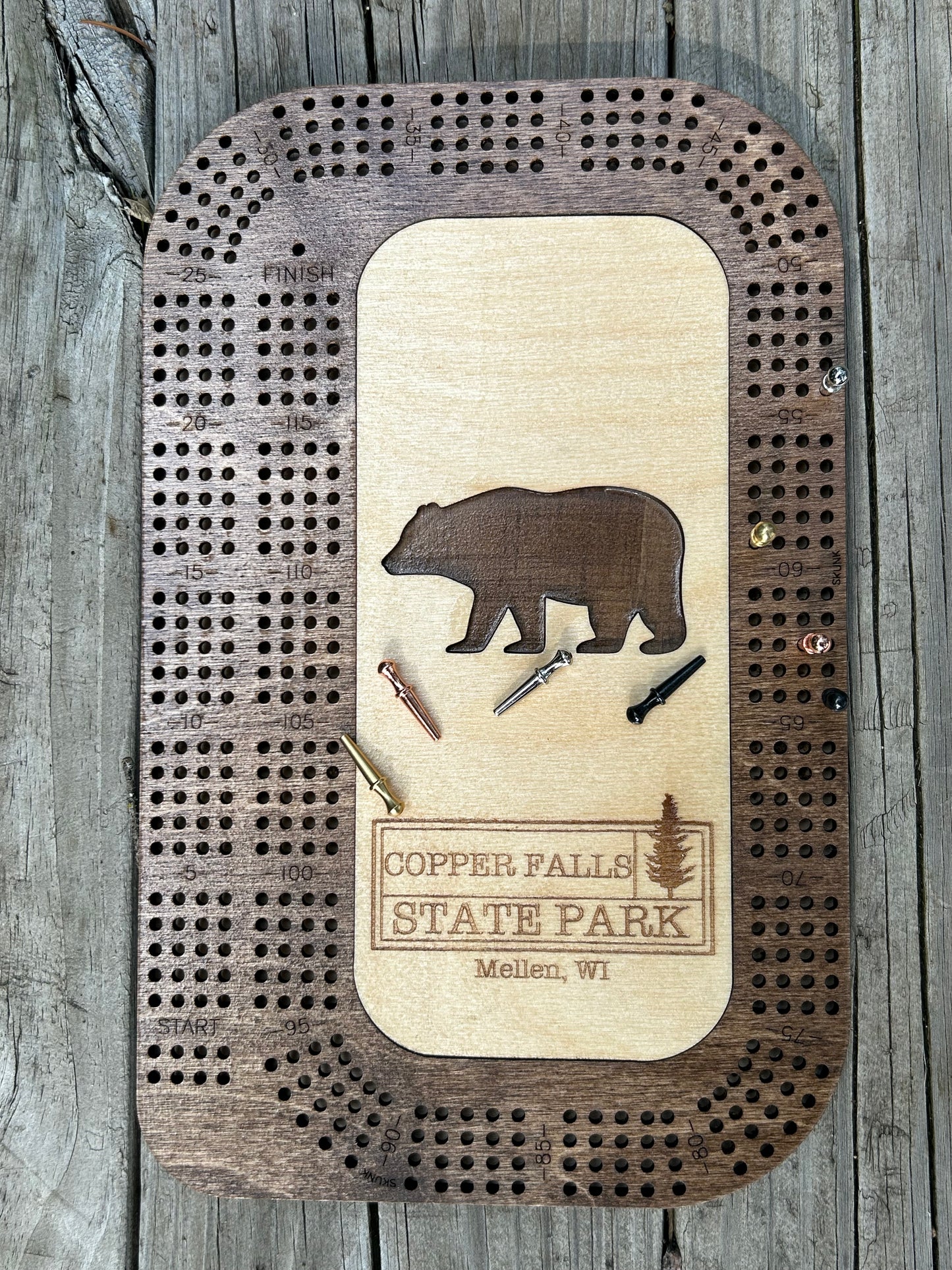 Wood cribbage board with a bear shaped cutout and Copper Falls State Park Text.  With eight metal pins. 