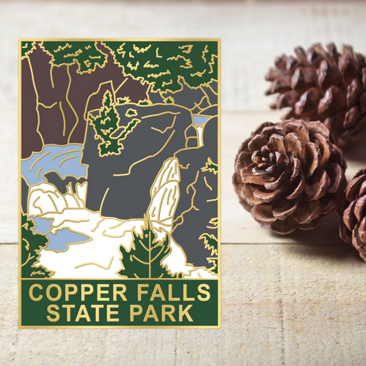Hard enamel pin depicting Copper Falls at Copper Falls State Park.  Photo background: rough sawn wood and pinecones.