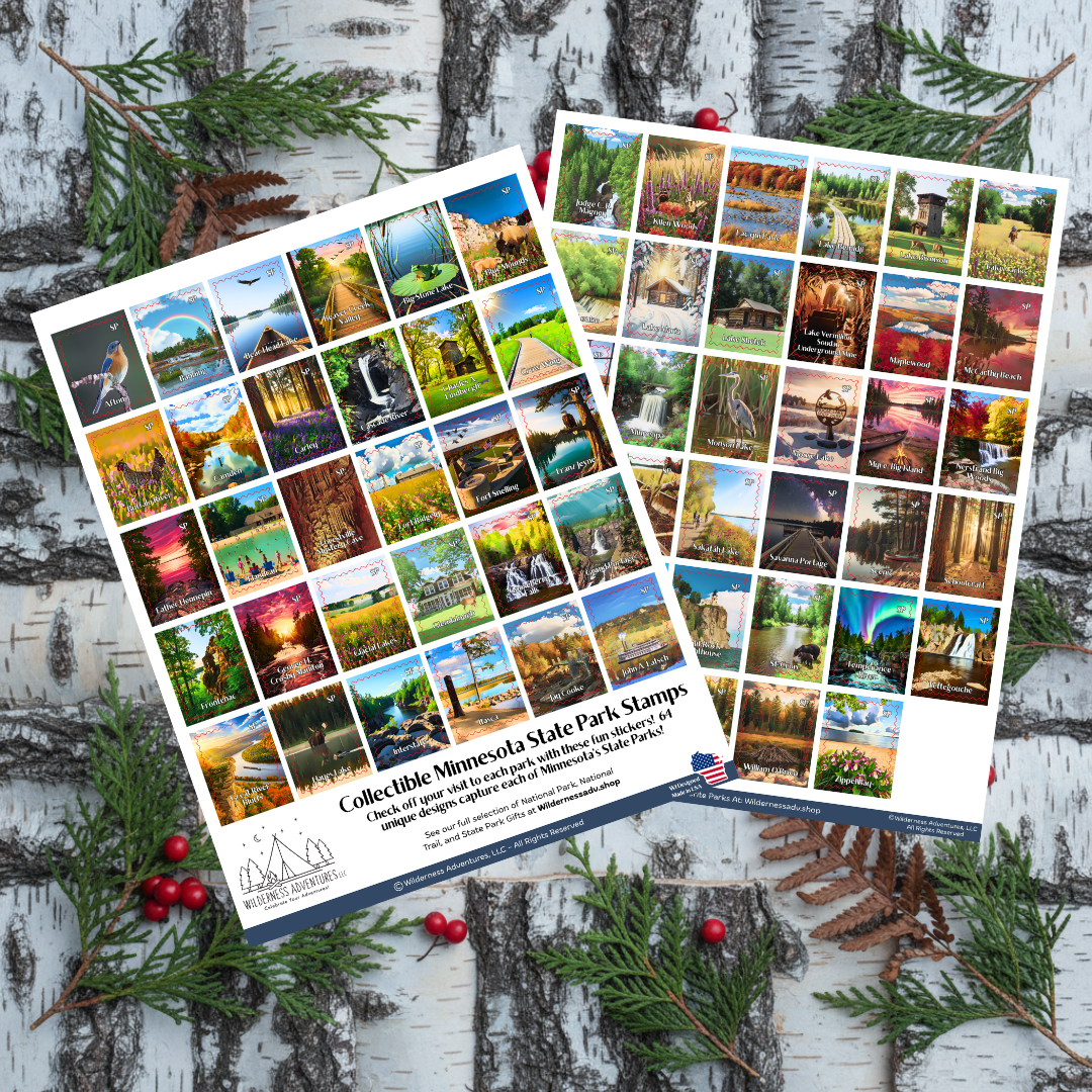 Two printed collectible Minnesota State Park stamps are arranged overlapping on a white birch wood surface with evergreen branches and small red berries. The stamps feature a grid of many scenic photographs and text at the bottom reading 'Collectible Minnesota State Park Stamps' with a website