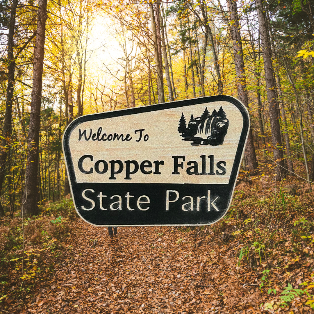 Wood grain acrylic magnet with “welcome to Copper Falls State Park” and waterfall icon.  Photo background: hiking trail through the woods in fall.