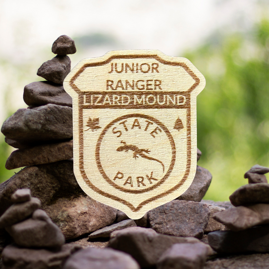 Wood Shaped badge with the text “Junior Ranger Lizard Mound State Park” and lizard symbol.  Photo background: stacked rocks.