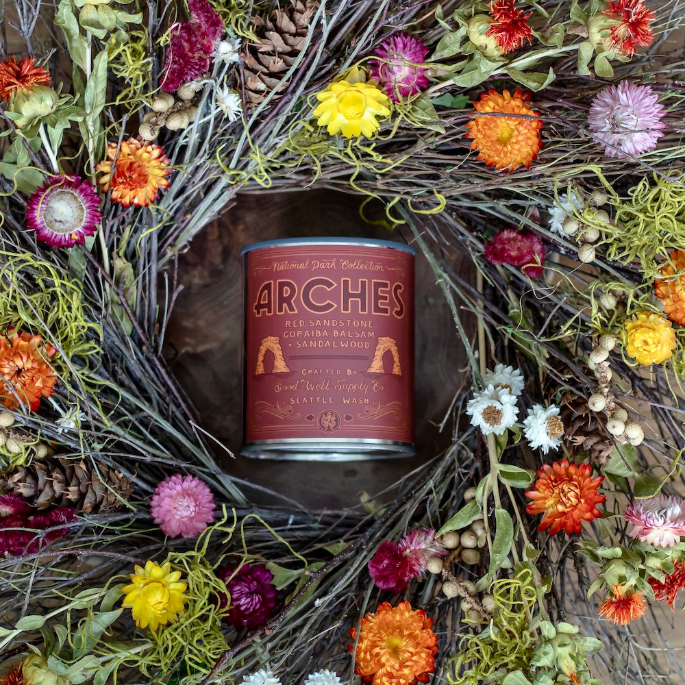 Arches lip balm surrounded by a decorative wreath with flowers and pine cones