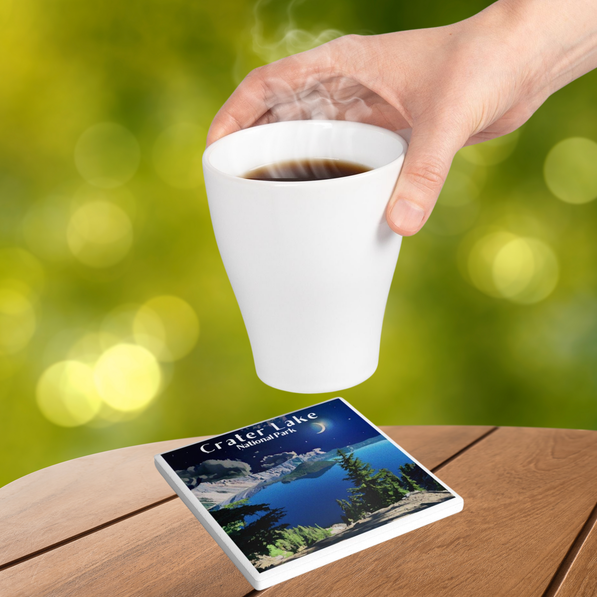 Ceramic coaster design featuring of the midnight sky over crater Lake and the text crater Lake national park.  Photo background: individual placing a hot beverage on the coaster that is sitting on a wood table.￼
