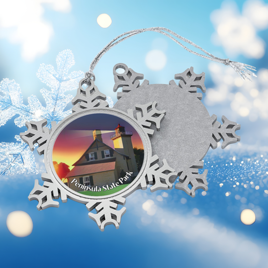 Silver snowflake-shaped ornament with a Peninsula State Park lighthouse design on a snowy background