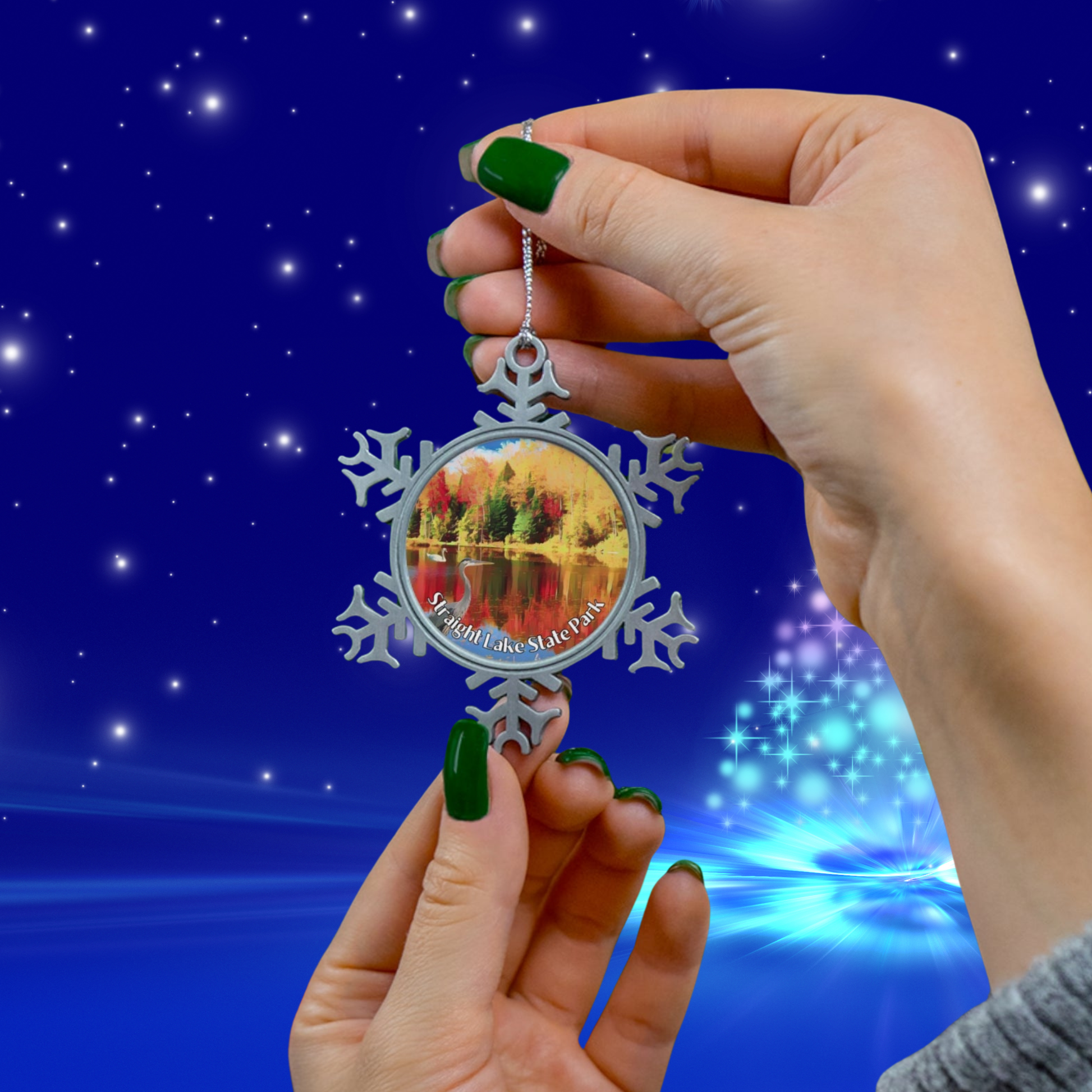 Hand holding a snowflake-shaped ornament with a scenic design against a starry night sky.