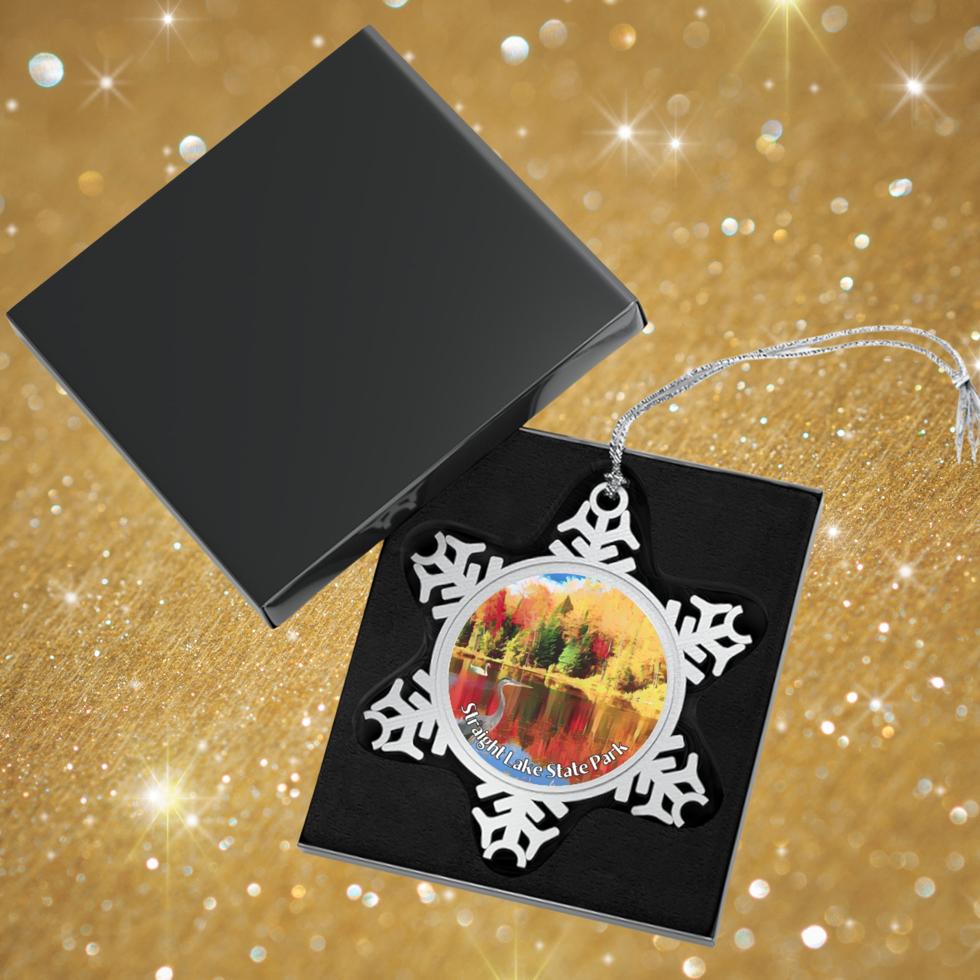 Snowflake-shaped ornament with a scenic design on a black card against a gold glittery background
