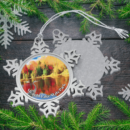 Decorative ornament with a scenic view of a lake surrounded by trees, placed on a wooden surface with pine branches.