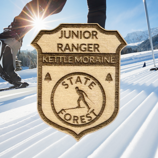 Wooden badge with 'Junior Ranger Kettle Moraine State Forest' text on a snowy background