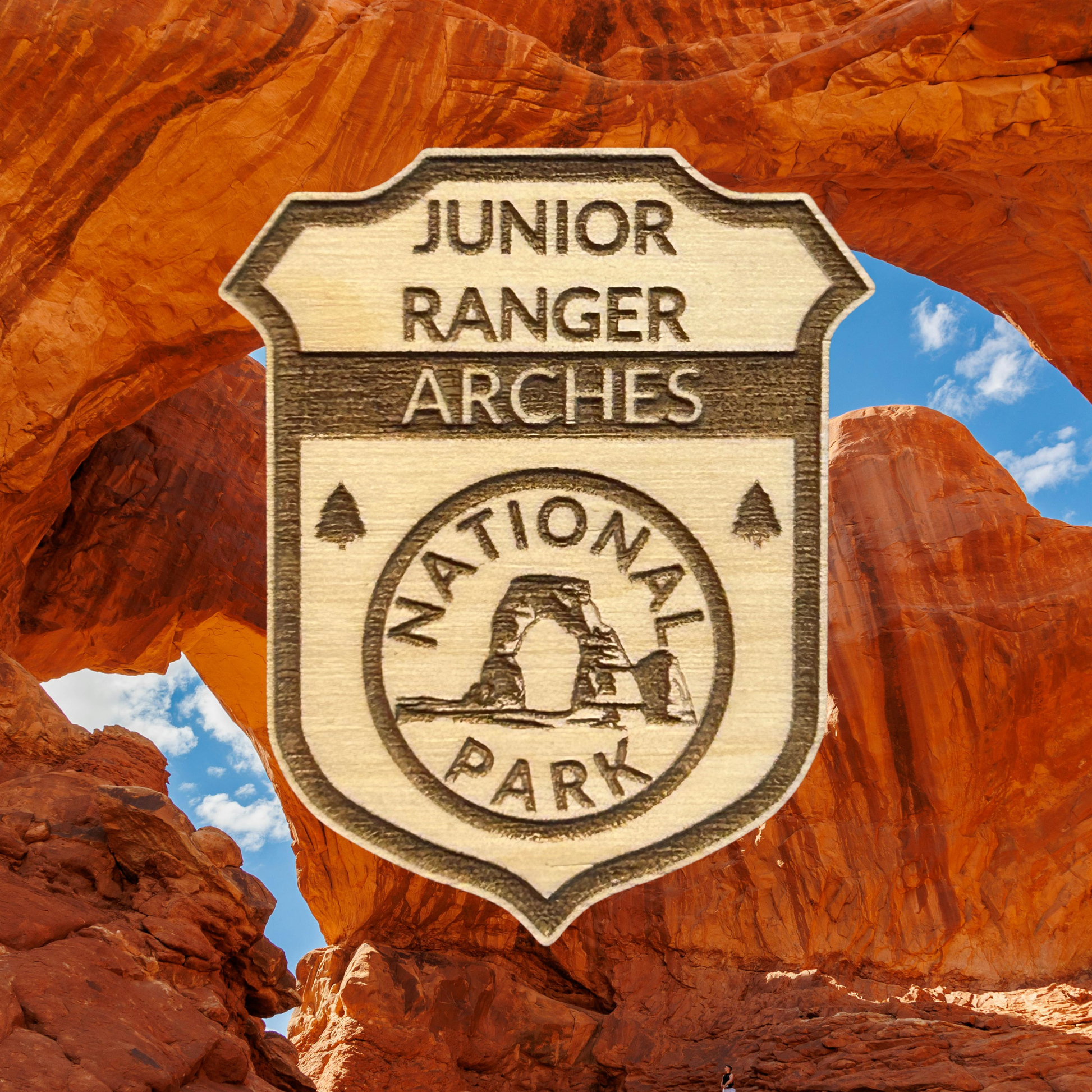 Junior Ranger Arches National Park badge against a desert landscape with rock formations.