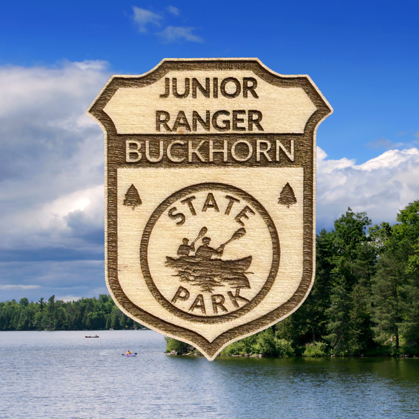 Wood badge with the text: “Junior Ranger Buckhorn State Park” set against a lake background.