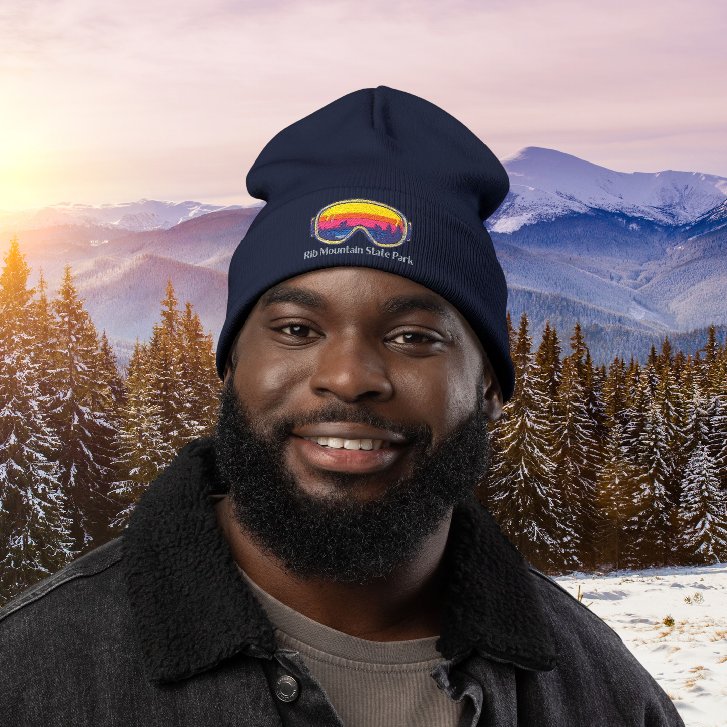Man wearing a beanie with colorful goggles design and Rib Mountain State Park text against a snowy mountain and forest background.