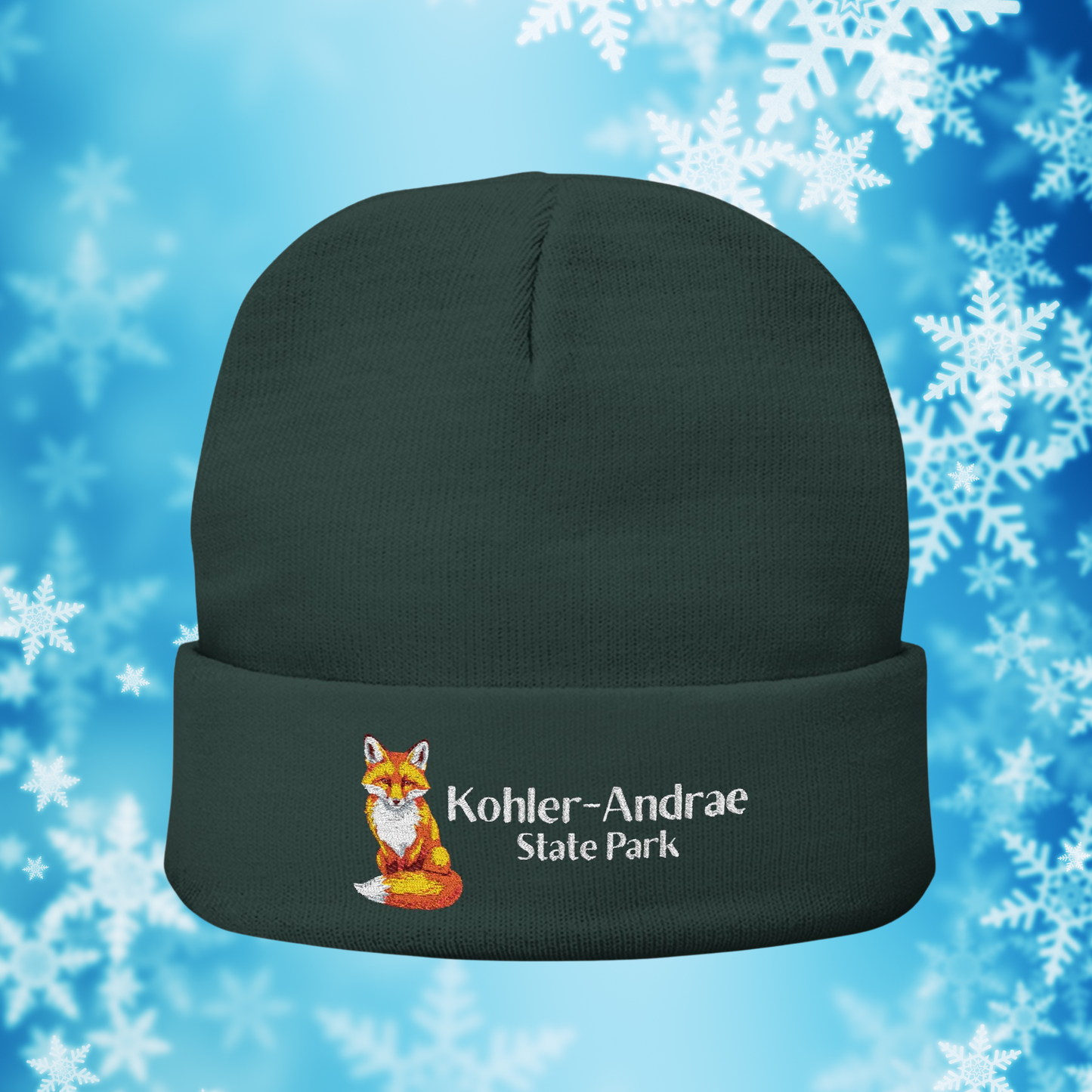 Dark Green  beanie with embroidered fox design and Kohler-Andrae State Park text text on a blue background with snowflakes
