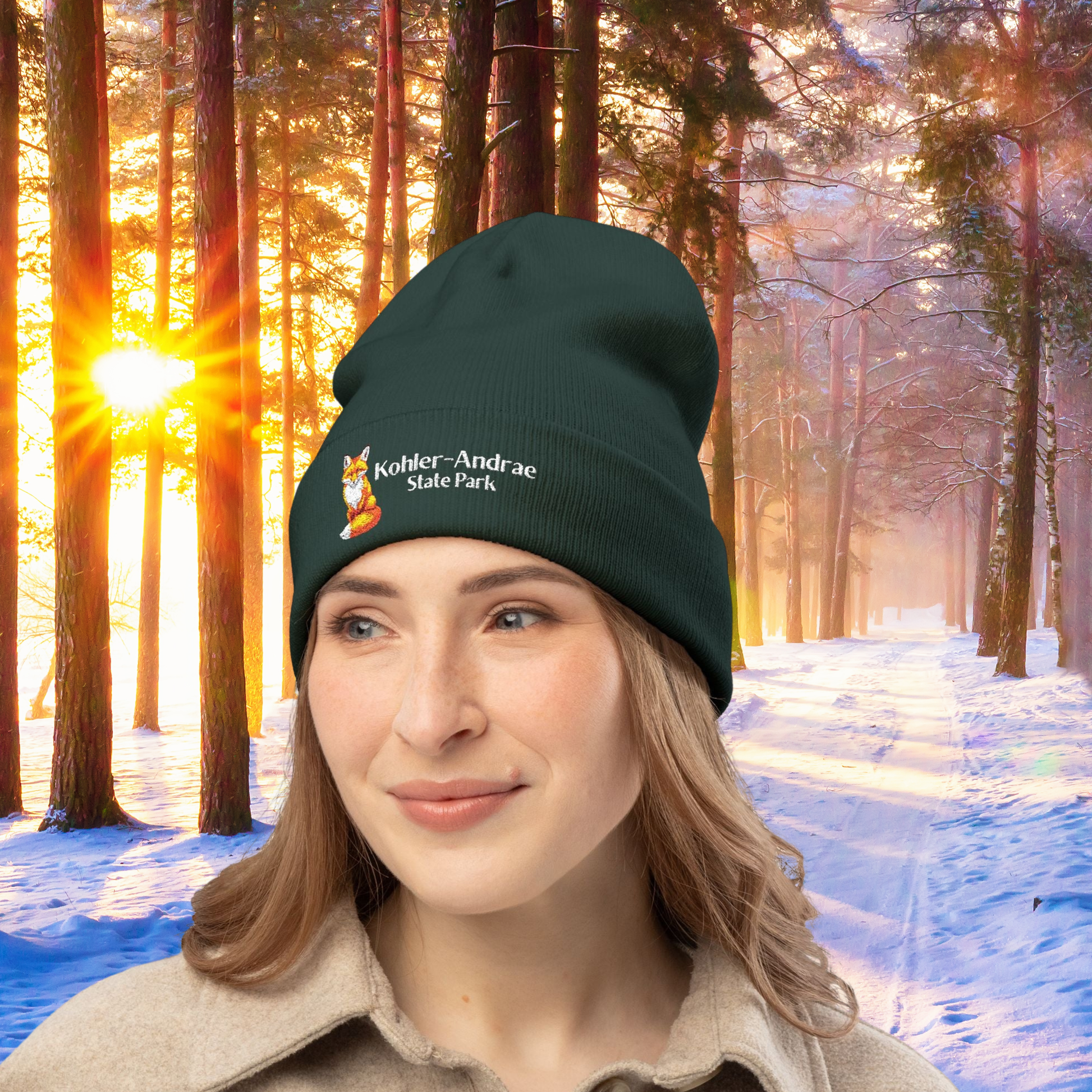 Woman wearing a dark green beanie with a Fox illustration and 'Kohler-Andrae State Park' text in a snowy forest setting