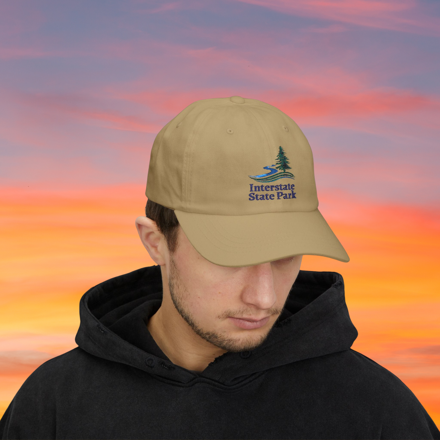 Person wearing a Khaki cap with 'Interstate State Park' logo against a colorful sky.