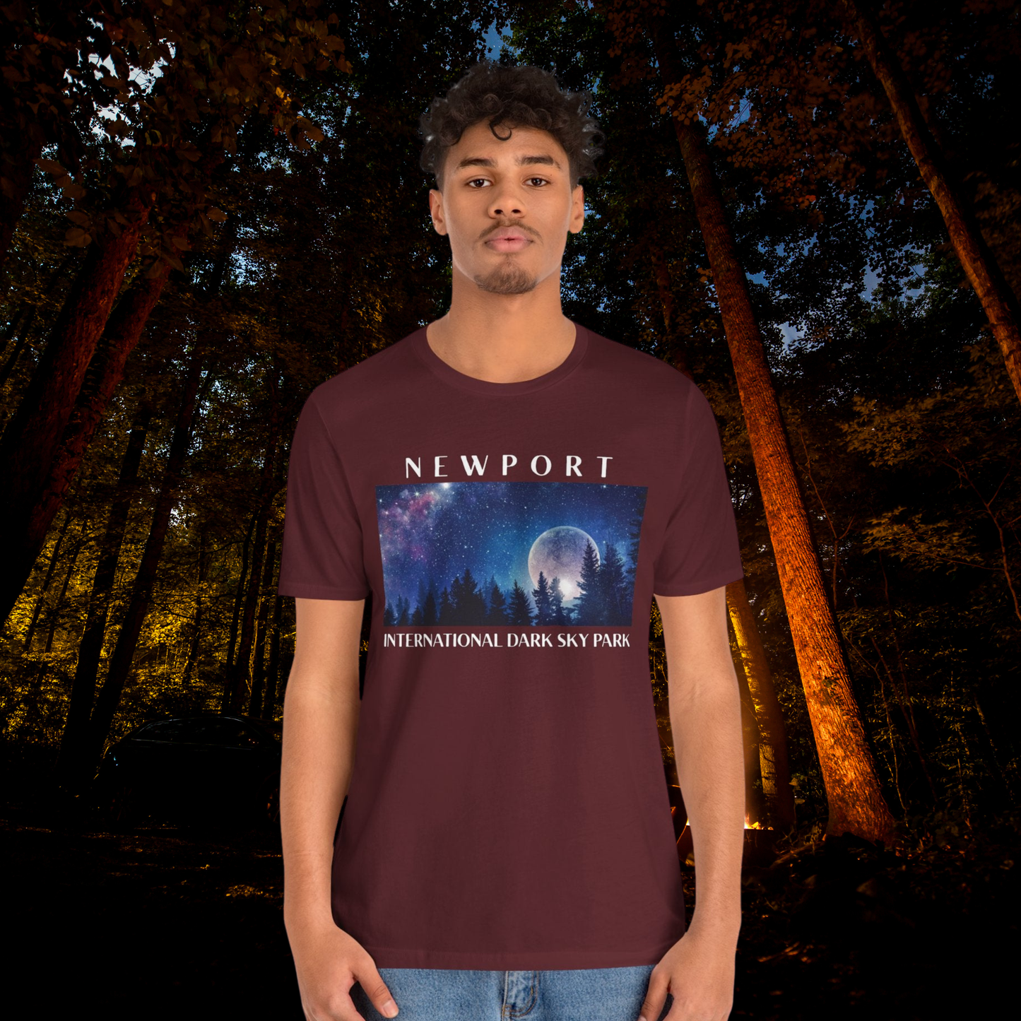 Person wearing a maroon t-shirt with 'Newport International Dark Sky Park' design in a forest setting