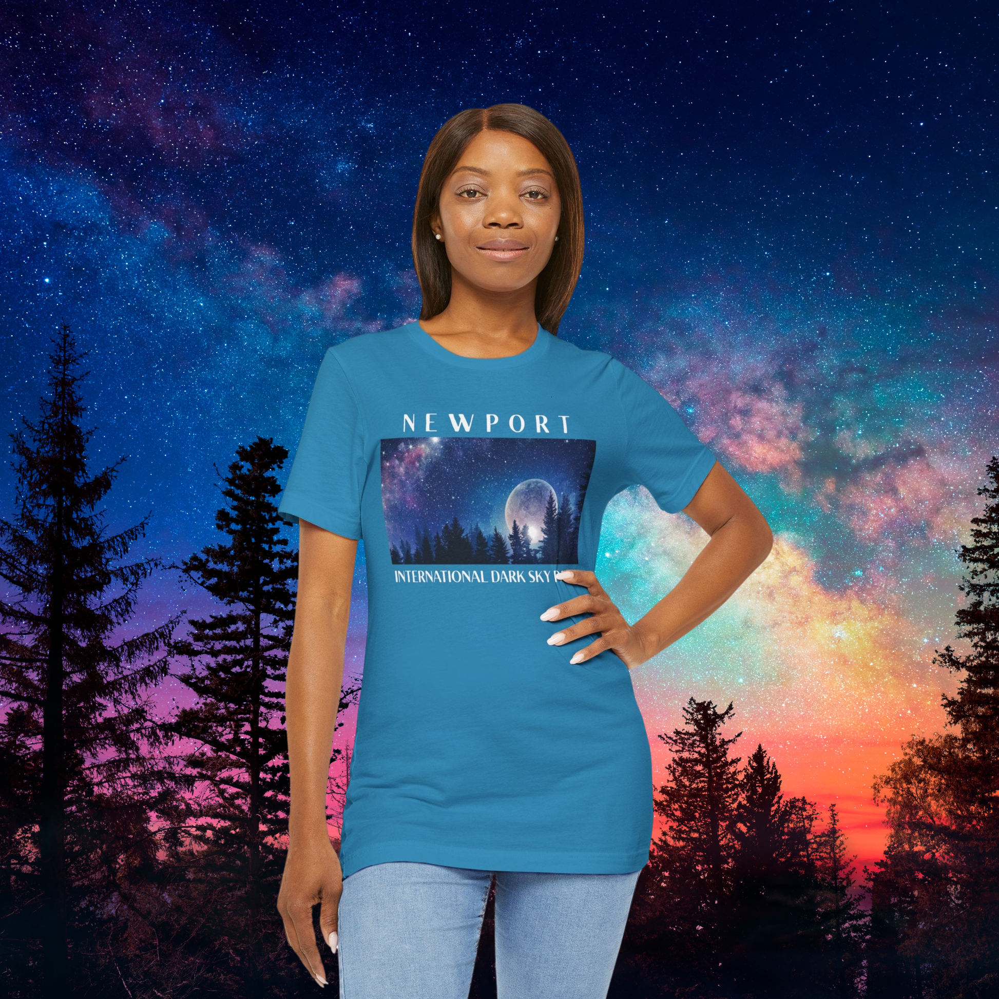 Person wearing an aqua blue t-shirt with 'Newport International Dark Sky' design against a colorful night sky background.