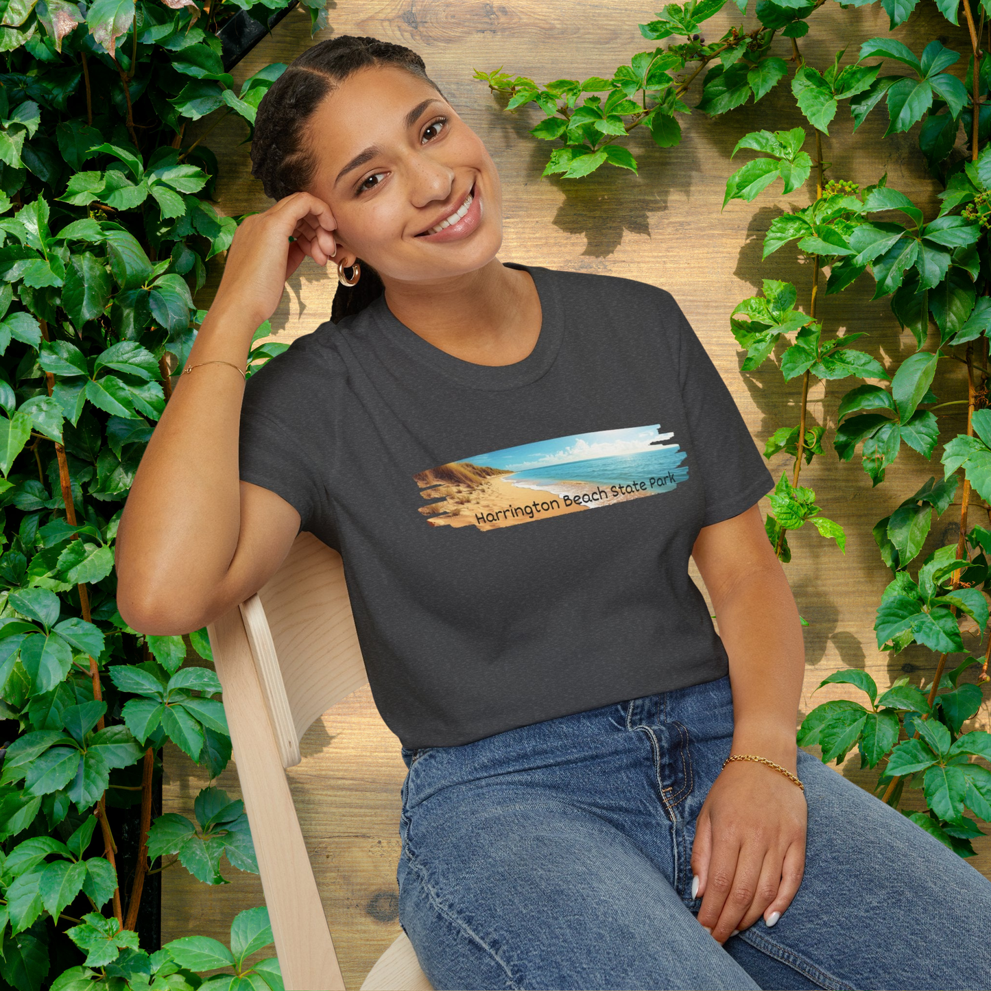 Woman wearing a dark heather t-shirt with a scenic design, sitting outdoors among greenery.