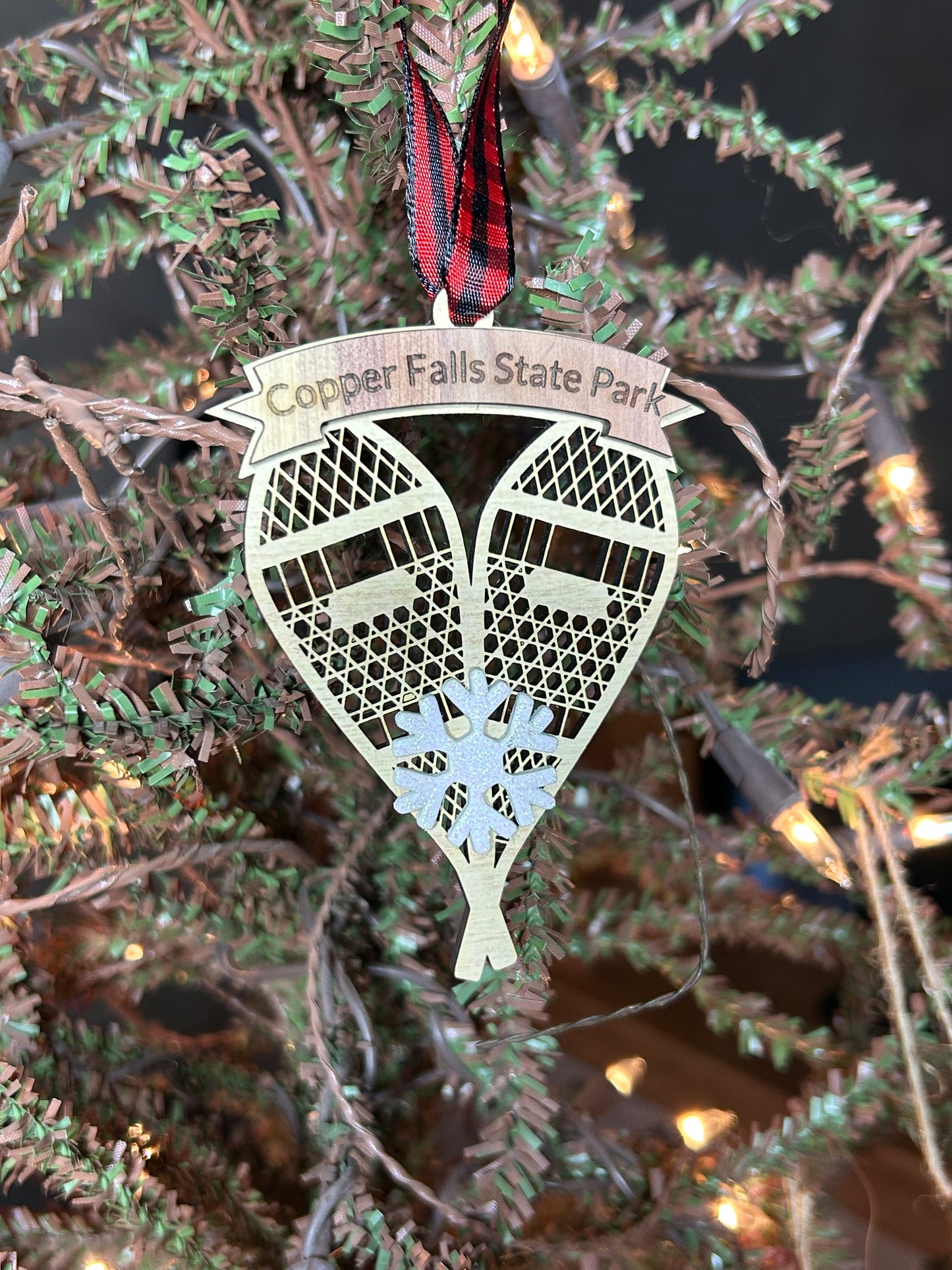 Ornament in the shape of snowshoes with decorative ribbon and snowflake on a Christmas tree background.