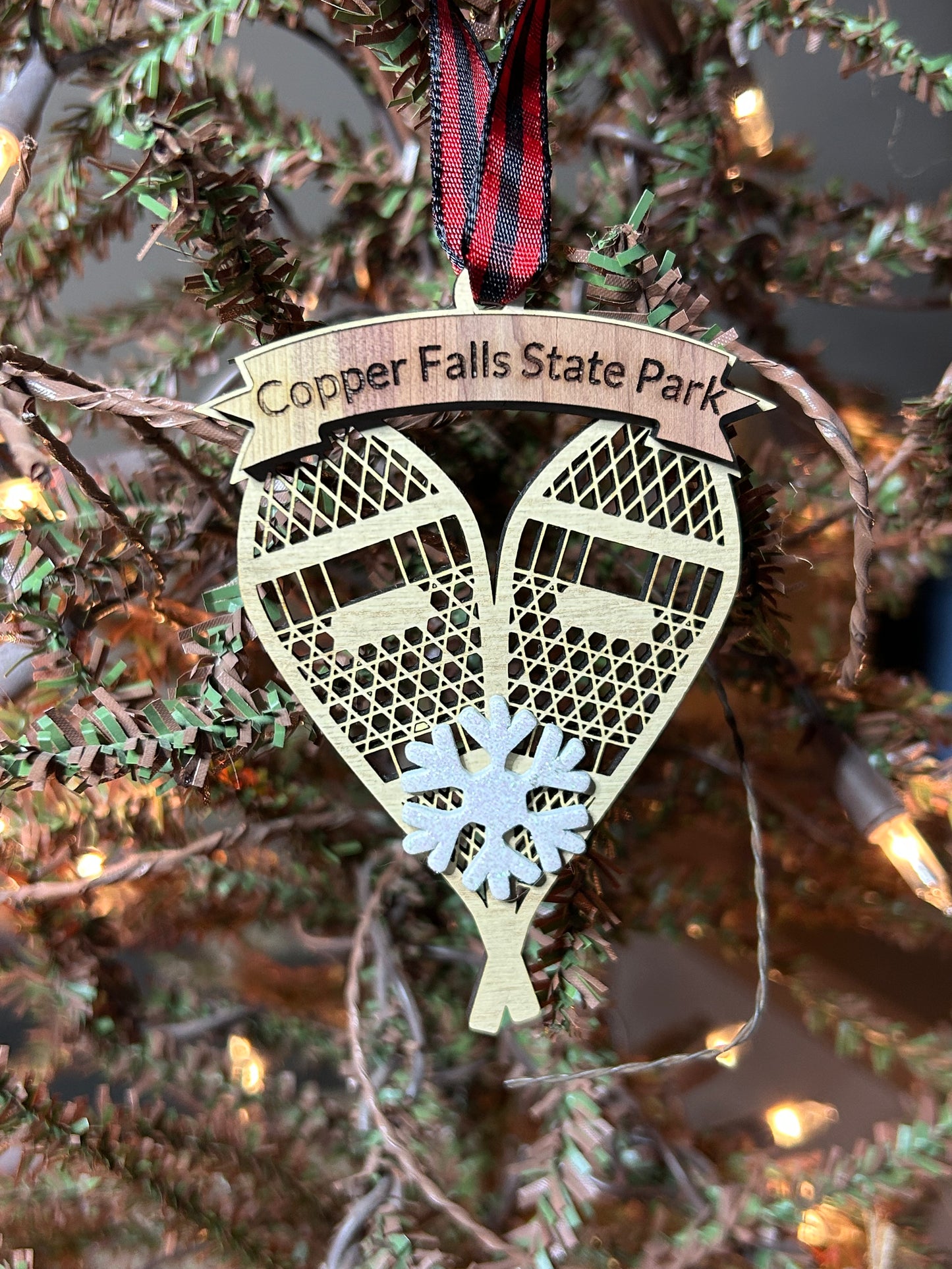 Ornament in the shape of snowshoes with decorative ribbon and snowflake on a Christmas tree background.