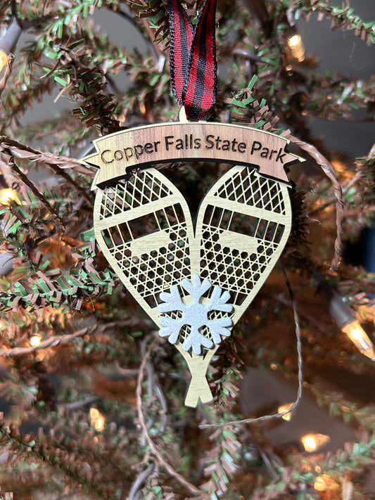 Ornament in the shape of snowshoes with decorative ribbon and snowflake on a Christmas tree background.