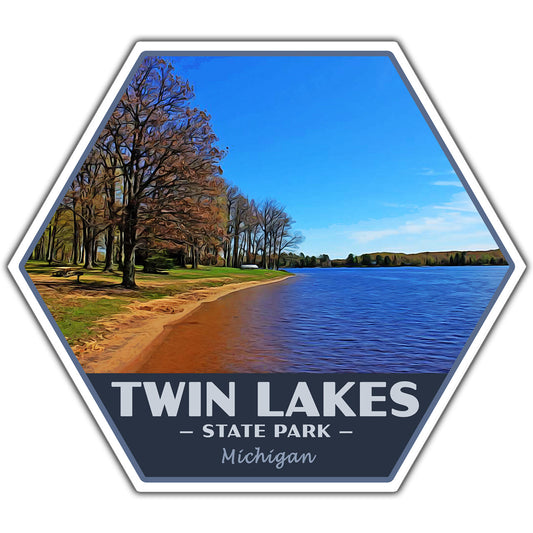 A hexagonal sticker featuring a scenic photograph of Twin Lakes State Park in Michigan, with a blue sky, lake, shoreline trees, and a dark blue banner reading “TWIN LAKES • STATE PARK • Michigan.”.